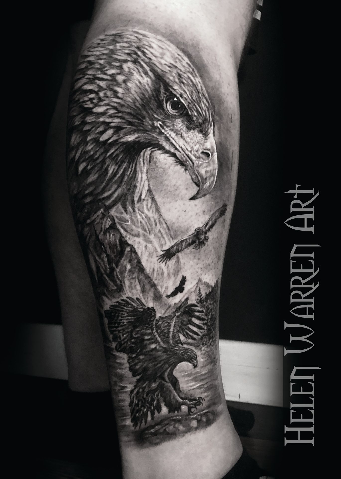 Realistic black and white eagle tattoo on a leg, with mountainous background, and eagles in flight.