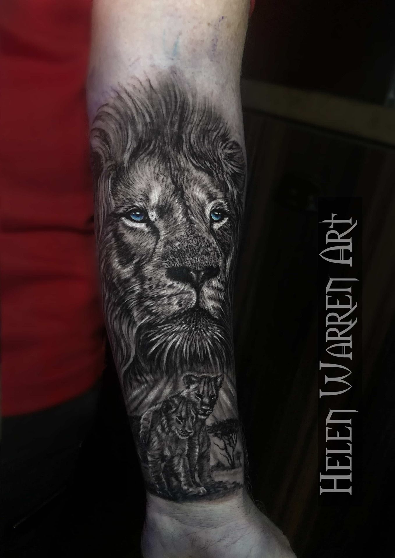 Tattoo of a lion's face and cub in black and white on an arm, done by Helen Warren Art.