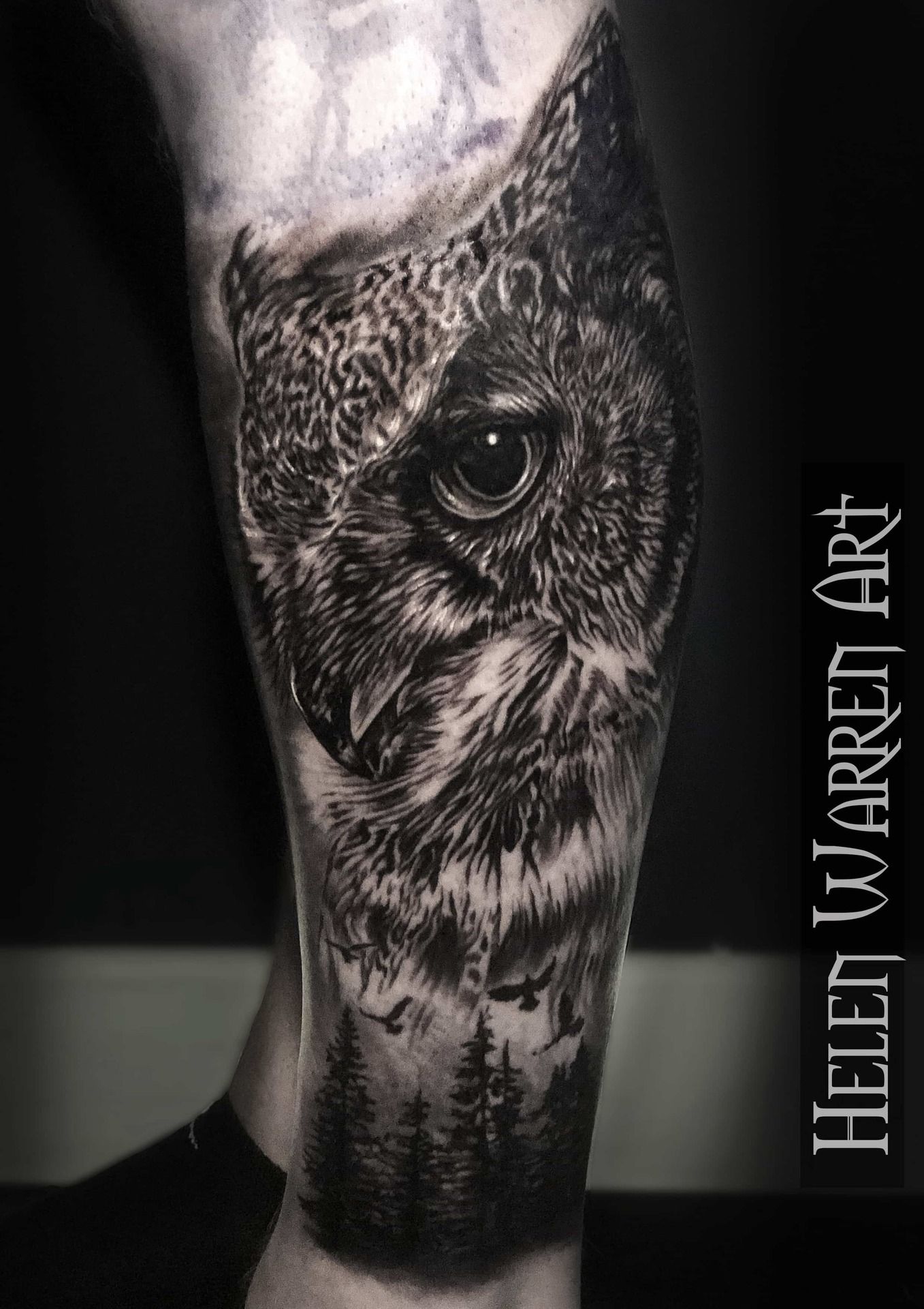 Black and white owl tattoo on leg, detailed shading. Forest scene at the bottom, artist name on the right.